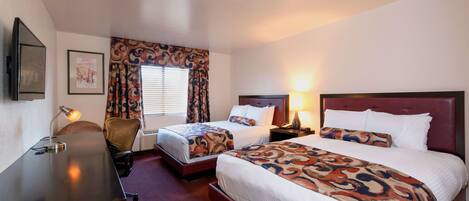 A hotel room with two beds, a desk, a chair, a TV, and a window with curtains.