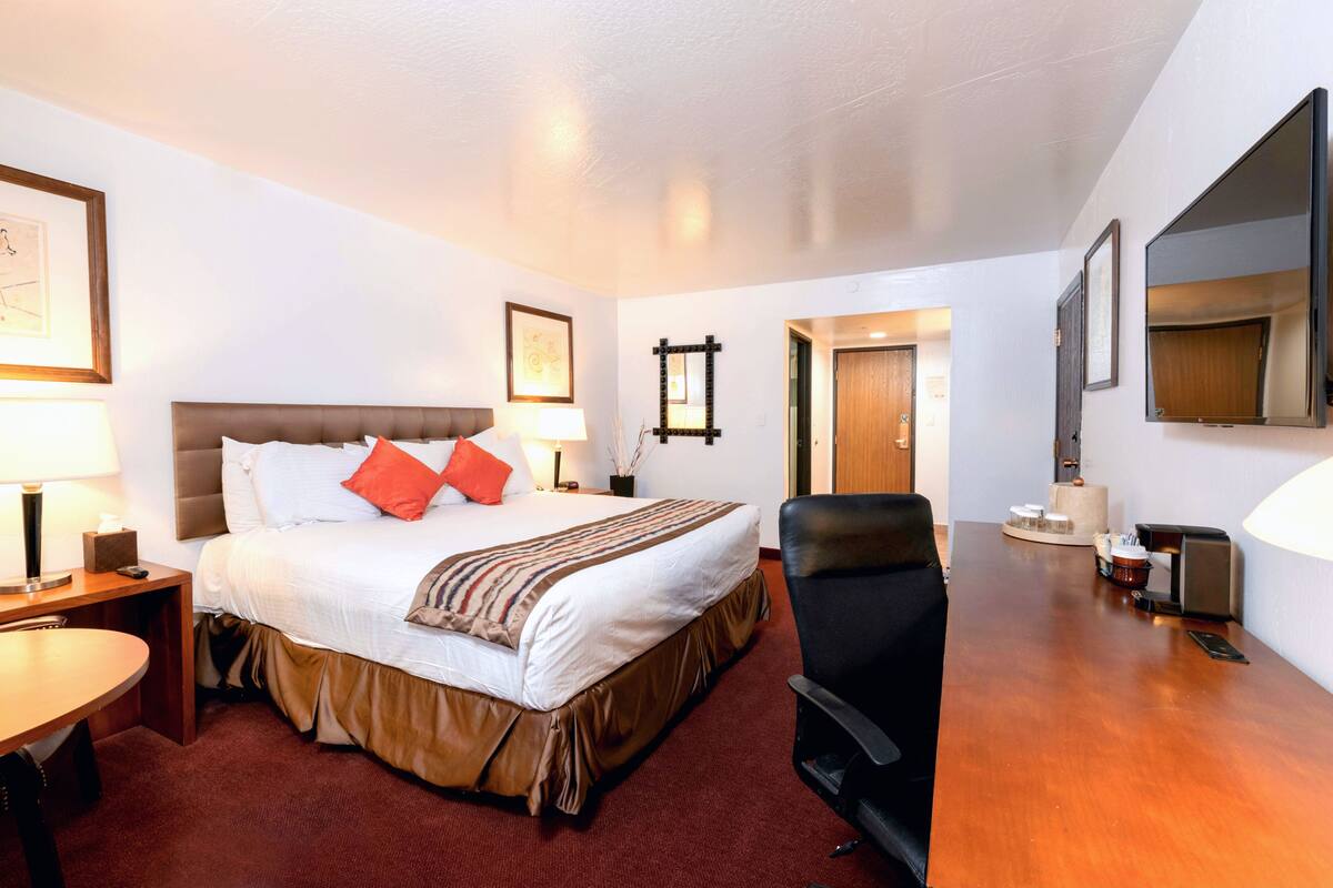 A hotel room with a large bed, a desk, a chair, and a TV.