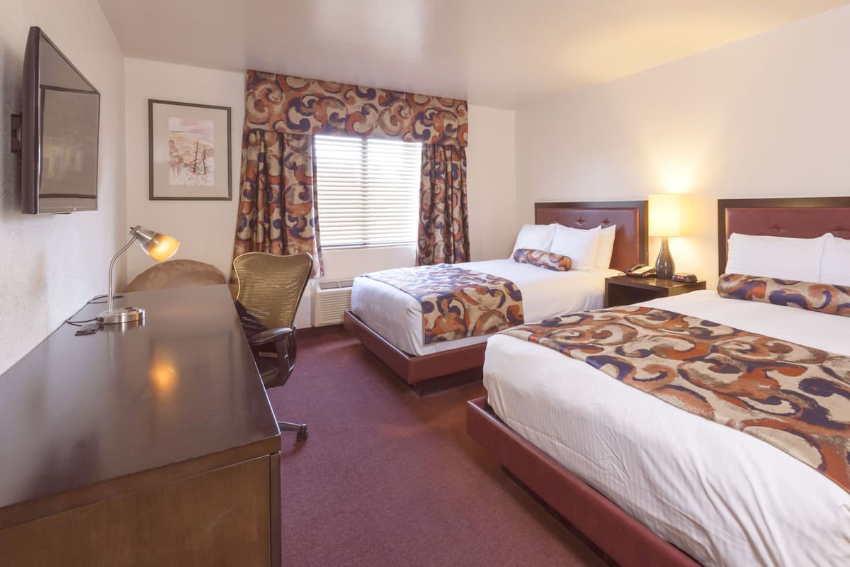 A hotel room with two beds, a desk, a chair, a TV, and a window with curtains.