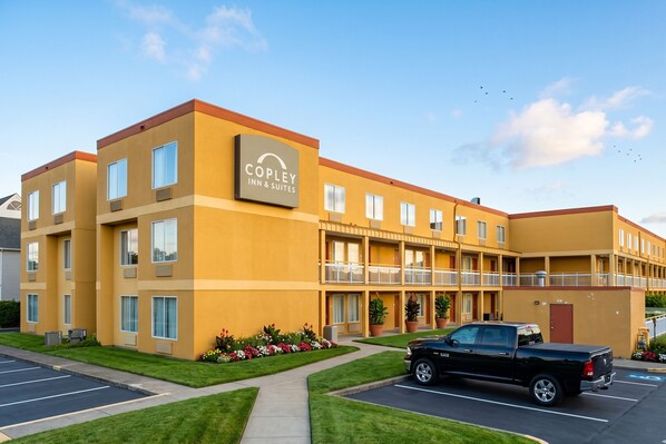 A hotel with a yellow facade, multiple balconies, and a parking lot.