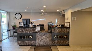 A hotel reception area with a reception desk labeled "INN" and "SUITES". There is a clock on the wall, a plant, and a sign indicating check-in times. - Copley Inn & Suites By OYO Akron OH (Akron)