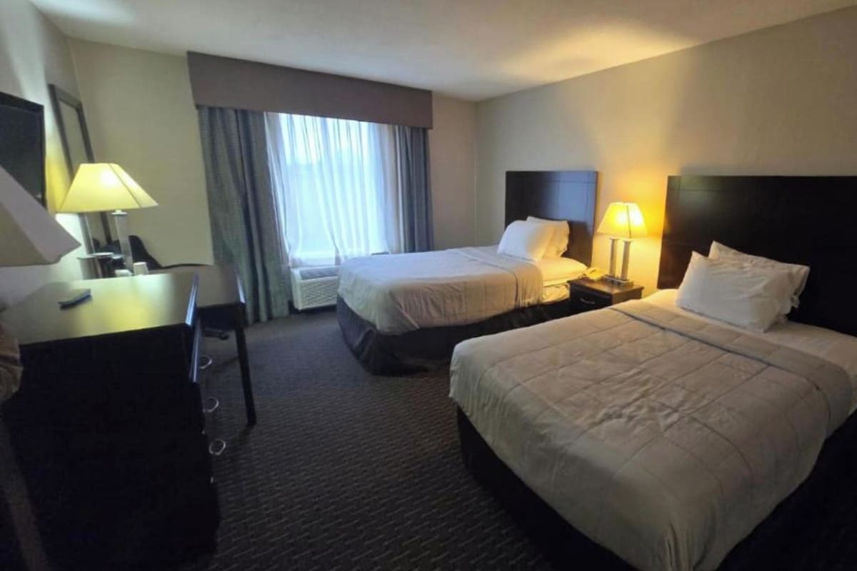 A hotel room with two beds, a desk, and a chair.