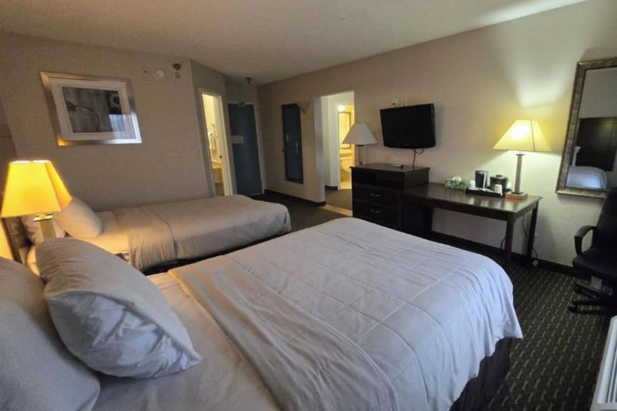 A hotel room with two beds, a desk, a television, and a mirror.