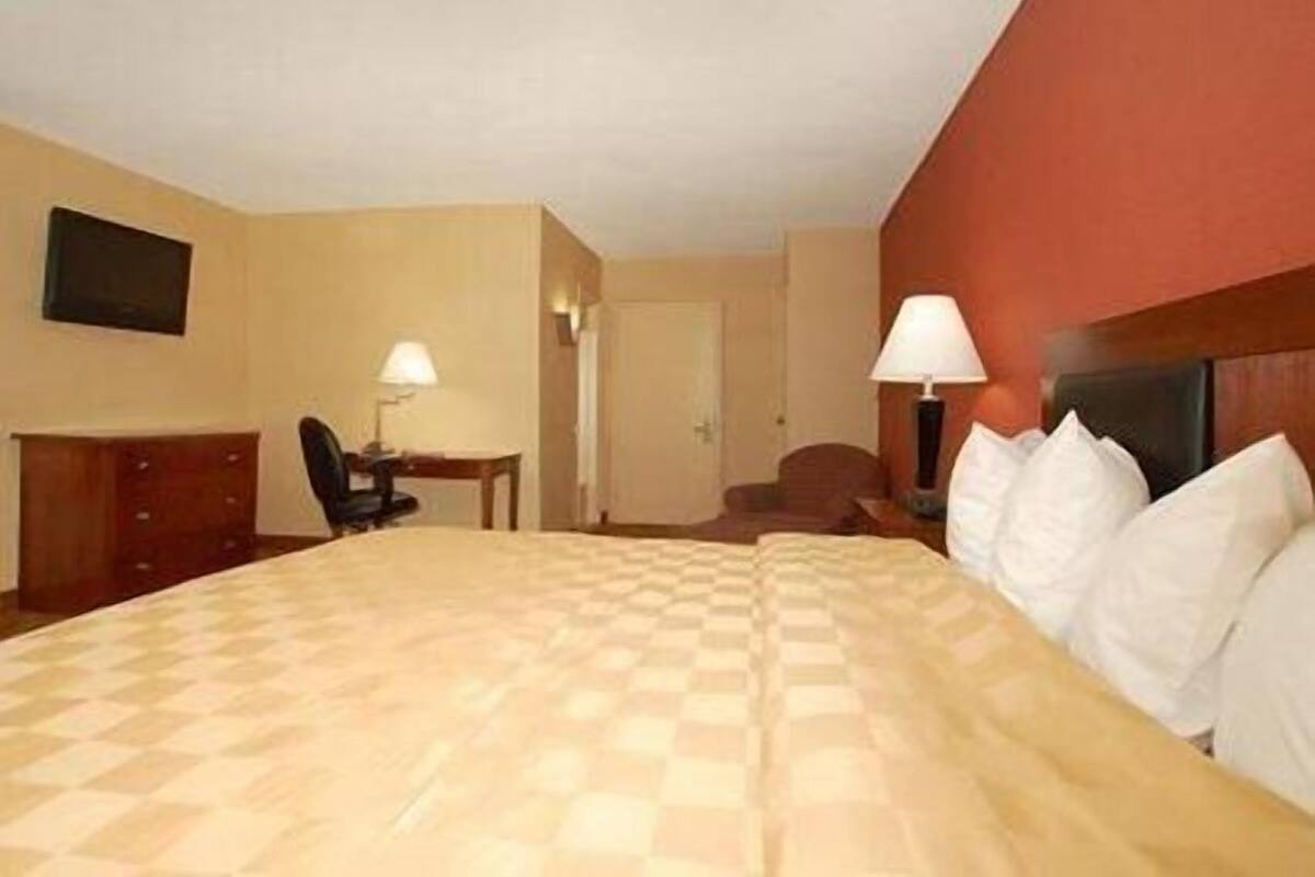 A hotel room with a large bed, a desk, a chair, and a lamp.