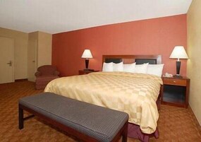 Una habitación de hotel con una cama, dos mesitas de noche, un banco y una silla.