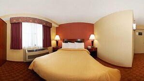 A hotel room with a large bed, two bedside tables with lamps, a window with curtains, and a built-in heater. - The Landing at Laguardia (East Elmhurst)