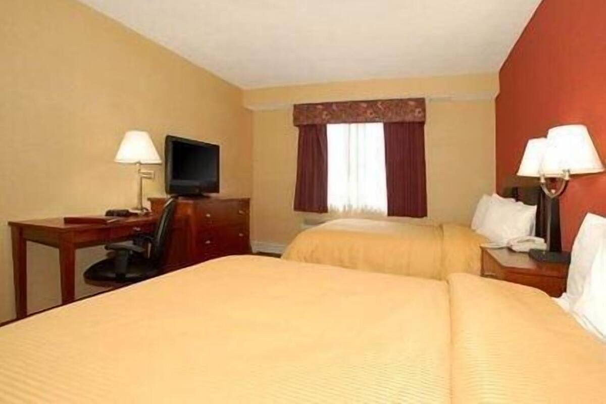 A hotel room with two beds, a desk with a lamp, a television, and a window with curtains.