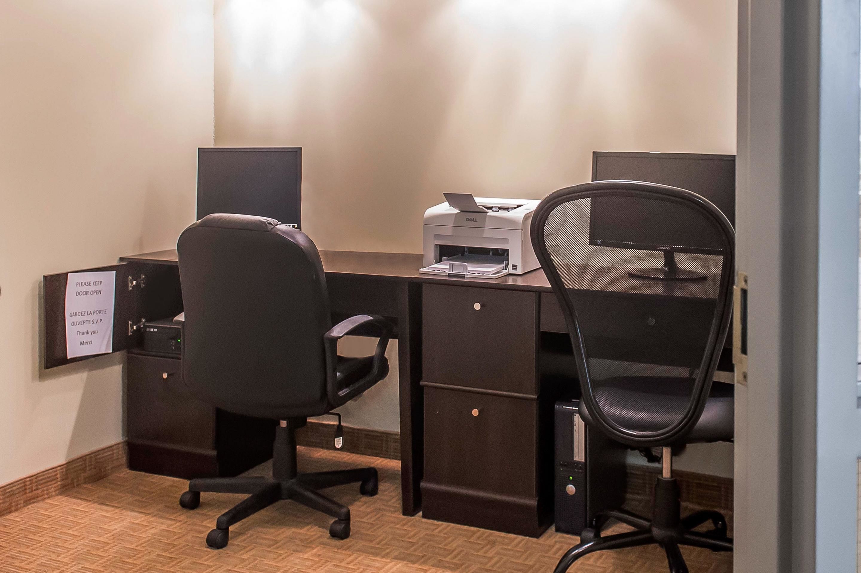 A hotel office with two desks, chairs, a printer, and a sign on the wall.