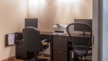 A hotel office with two desks, chairs, a printer, and a sign on the wall.