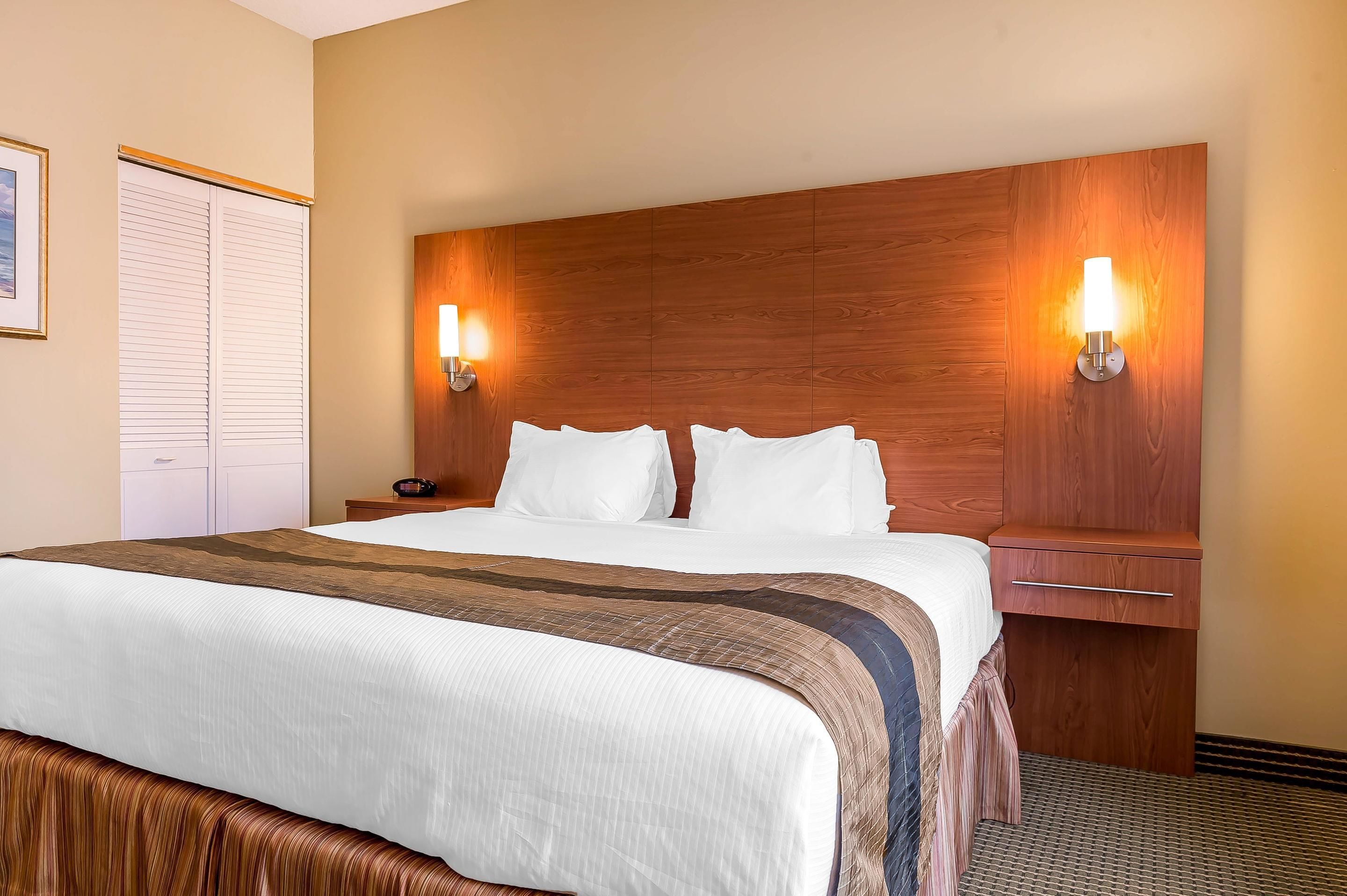 A hotel room with a large bed, two bedside tables, a wooden headboard, and two wall-mounted lamps.