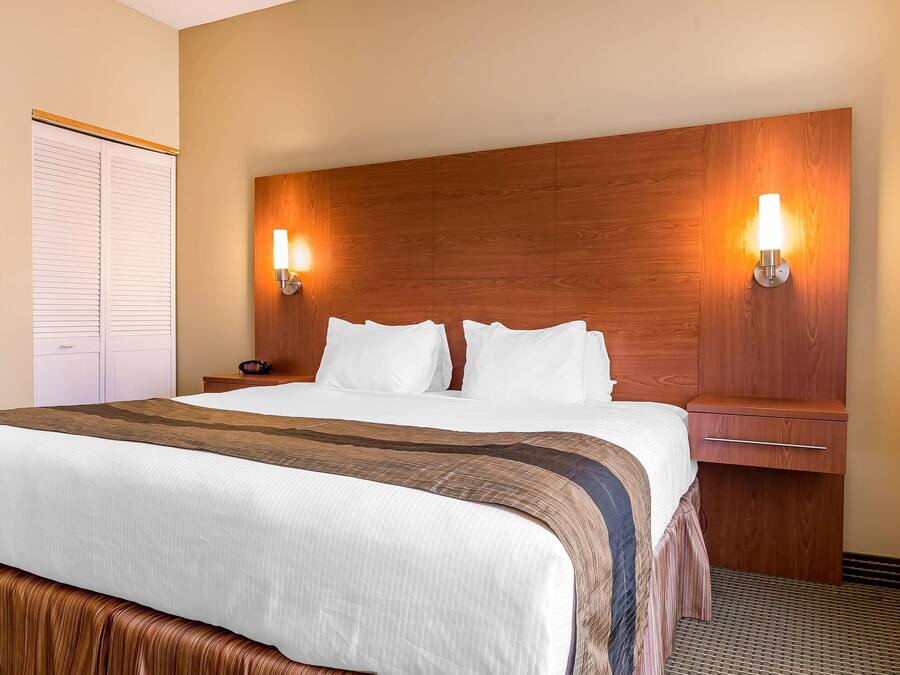 A hotel room with a large bed, two bedside tables, a wooden headboard, and two wall-mounted lamps.