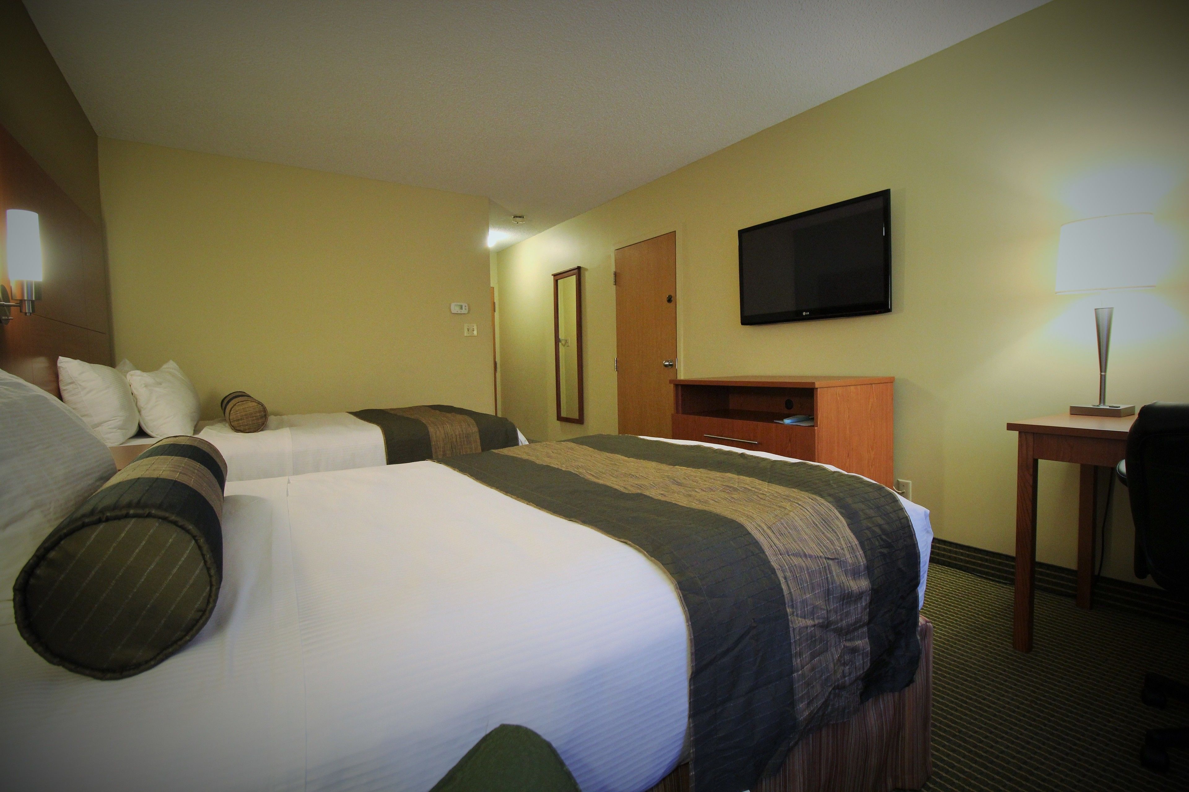 A hotel room with two beds, a television, a desk, and a lamp.