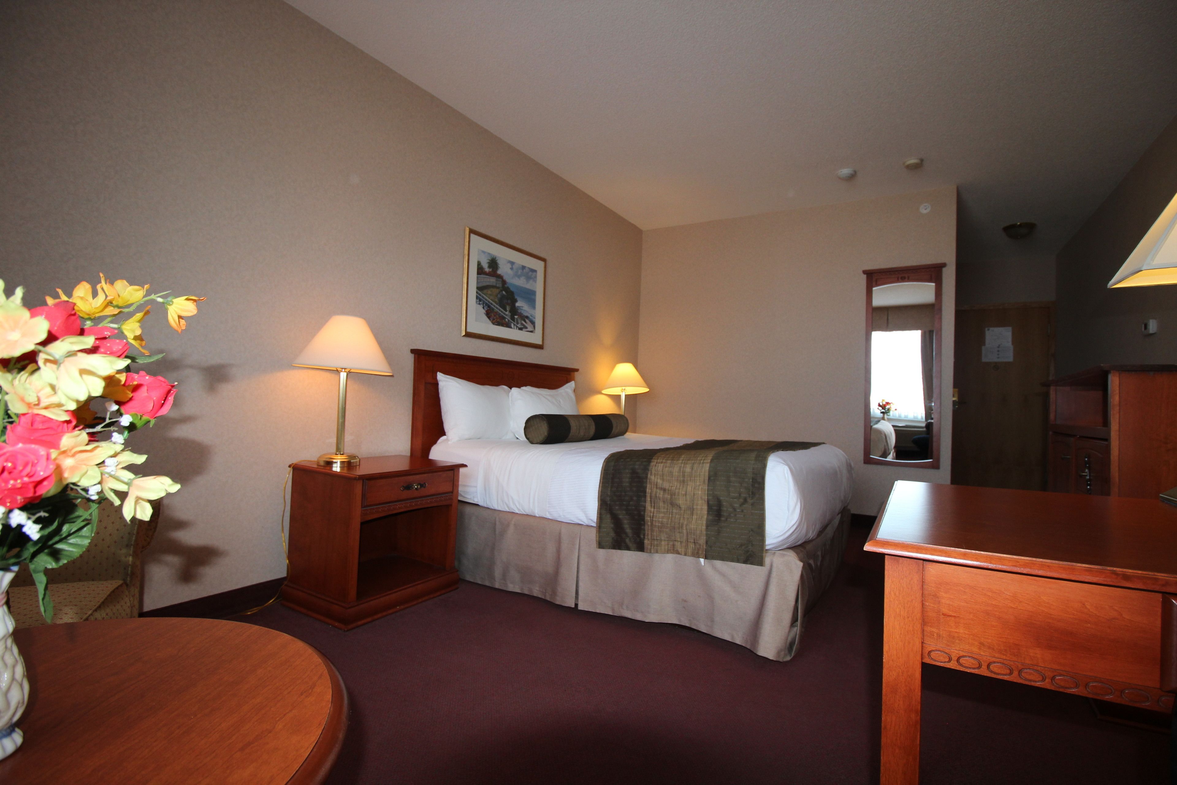 Habitación de hotel con cama, lámparas de noche, mesita de noche de madera, escritorio y espejo.