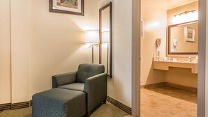 Un baño de hotel con una silla, un espejo grande y un lavamanos con tocador.