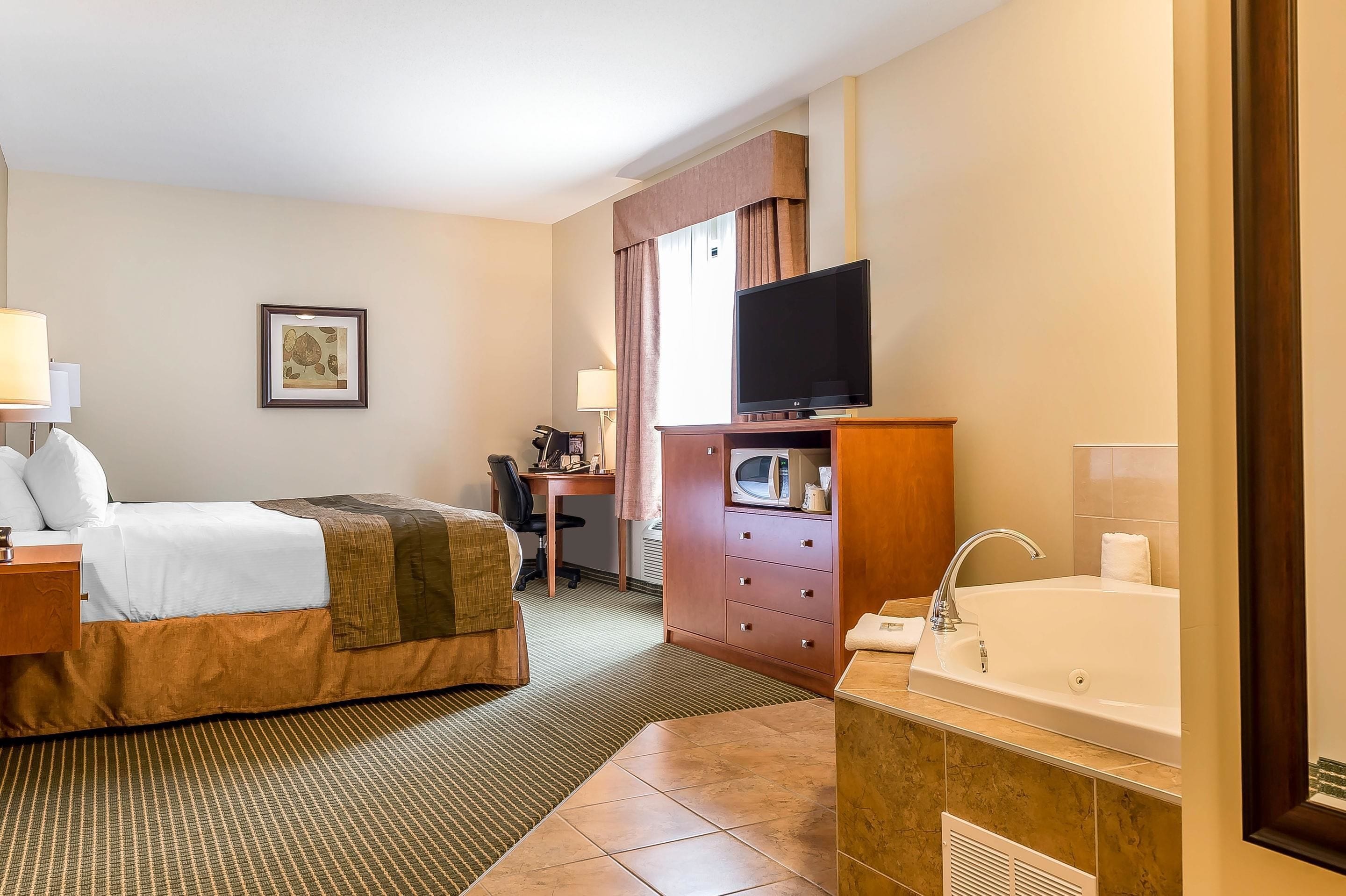 A hotel room with a bed, a desk, a television, a microwave, a sink, and a large window.
