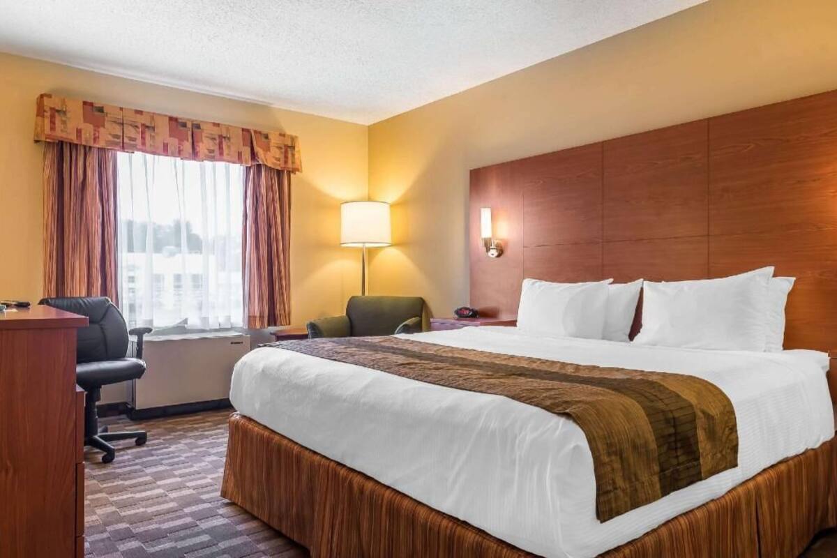 Habitación de hotel con una cama grande, un escritorio, una silla, una lámpara y vistas de la ciudad.