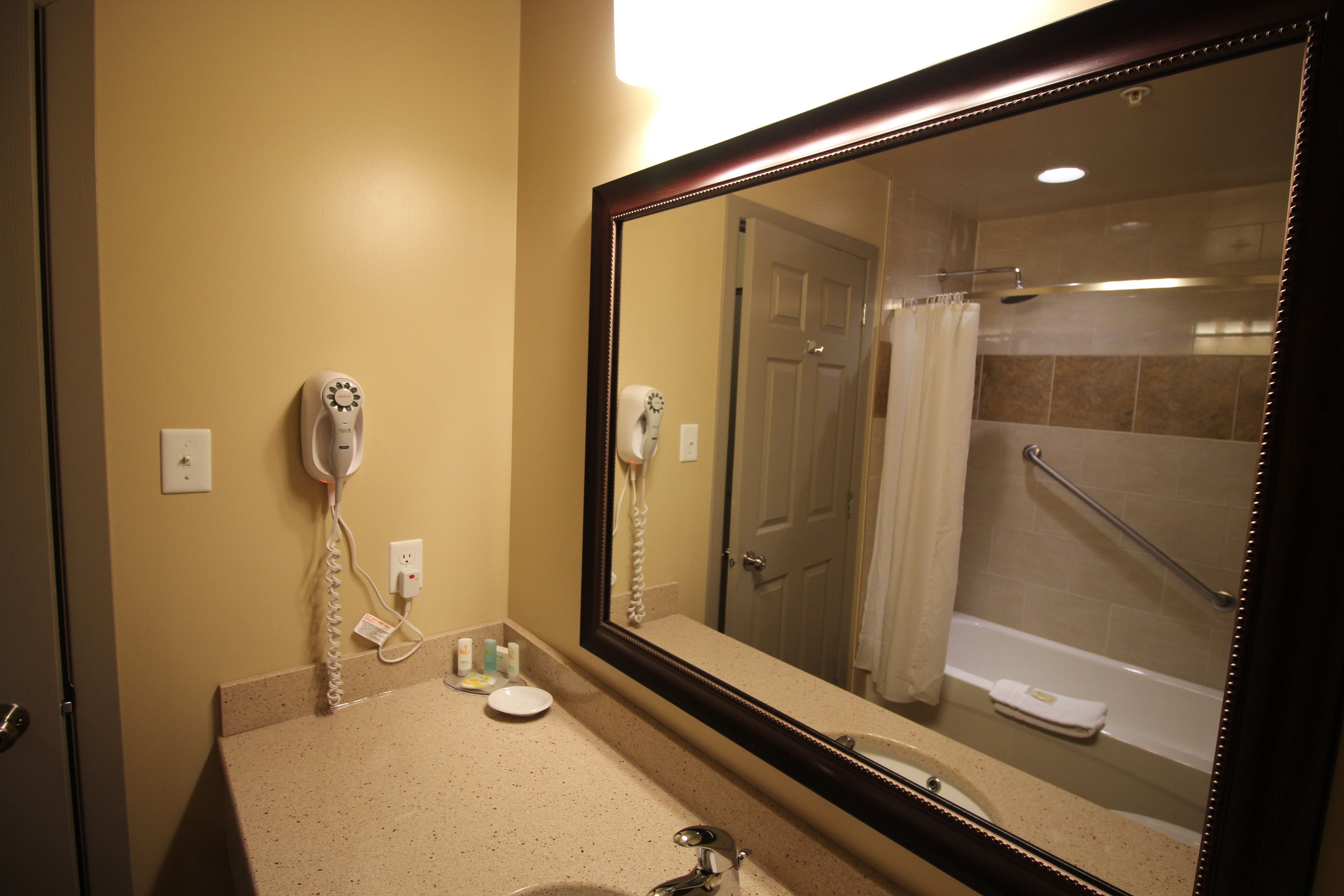 A bathroom with a large mirror, a hairdryer, a sink, and a bathtub.