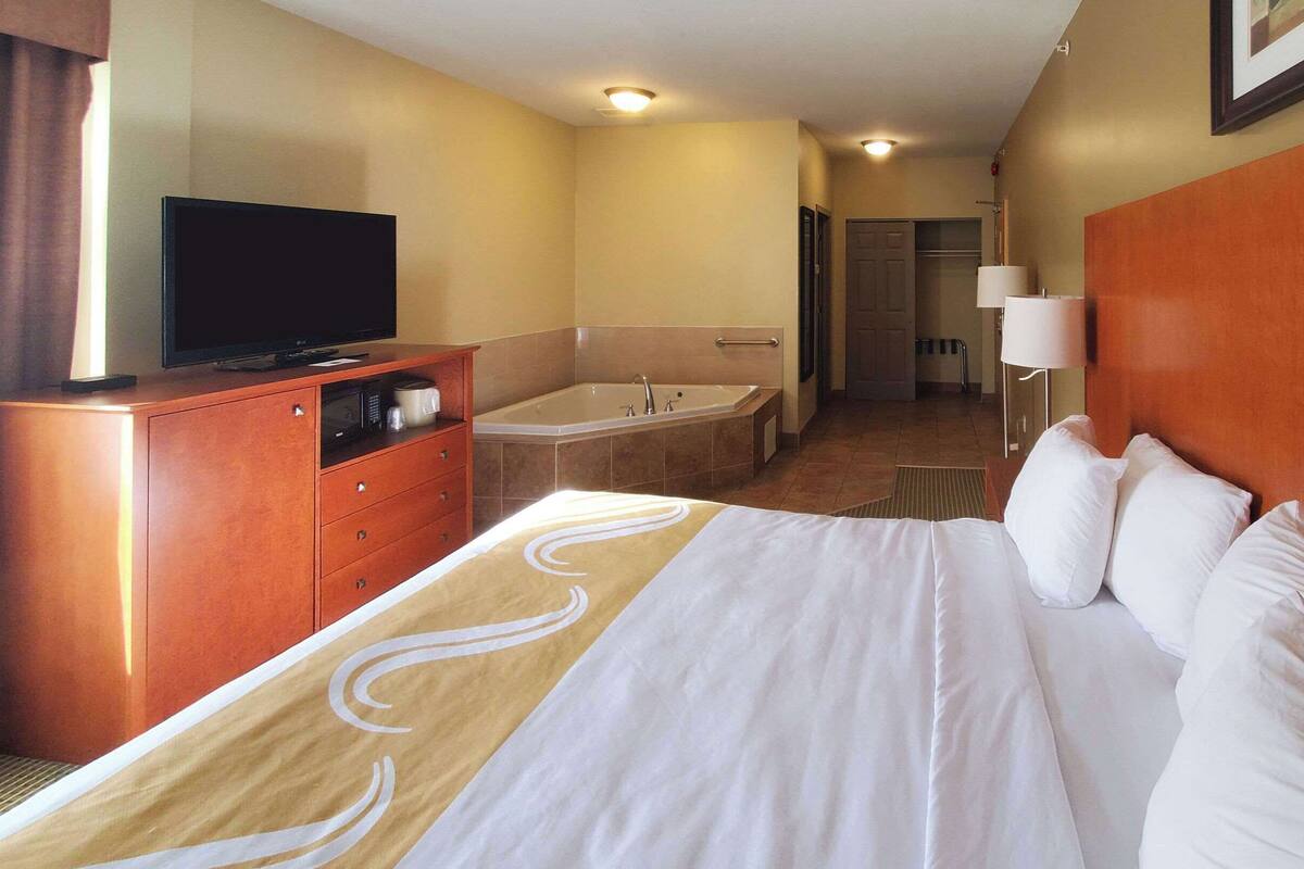 Une chambre d’hôtel comprenant un lit, une télévision, une salle de bain avec baignoire et un bureau avec une lampe.