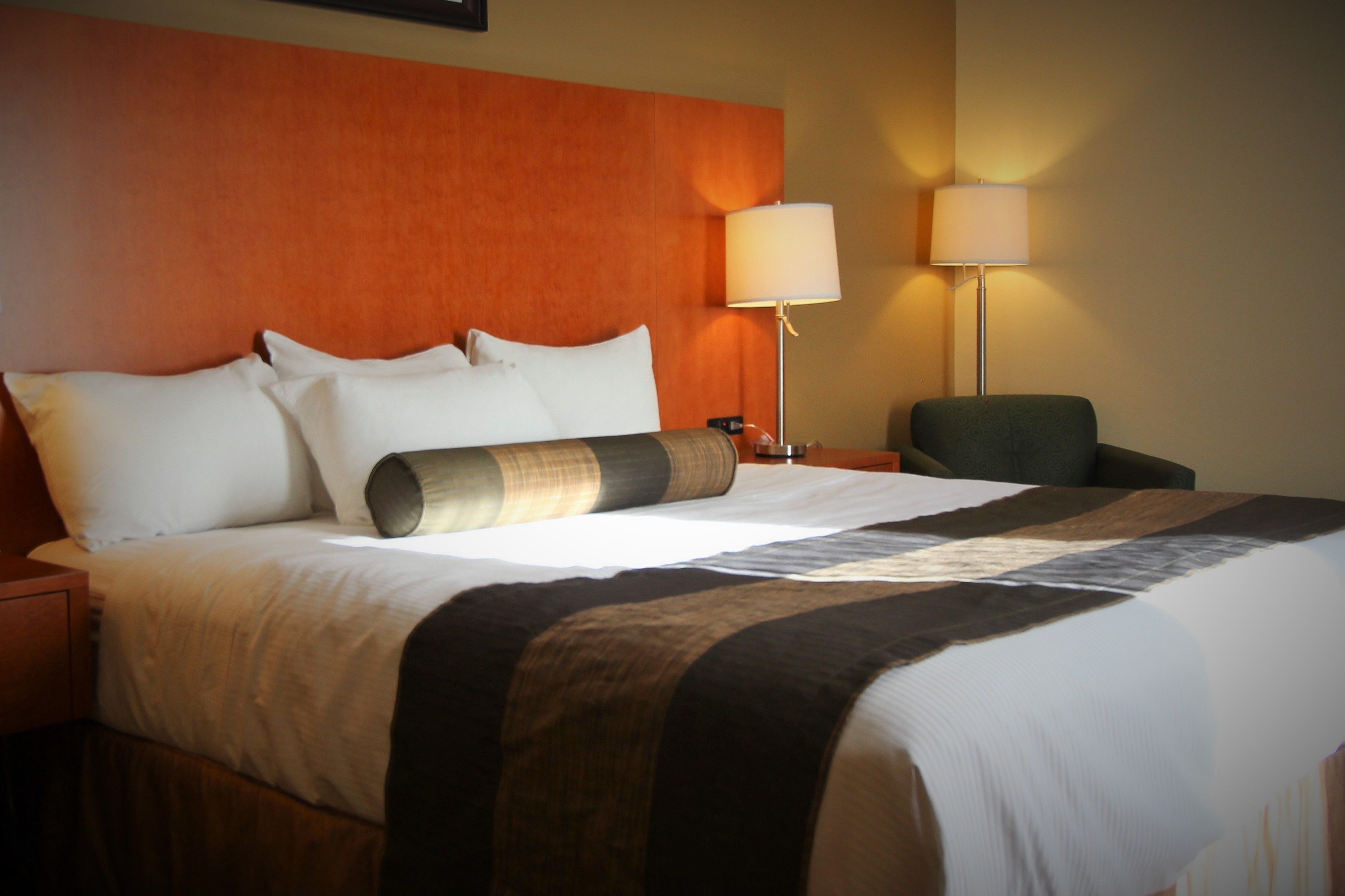 Una habitación de hotel con una cama grande, dos lámparas de noche, una silla y una mesita de noche.