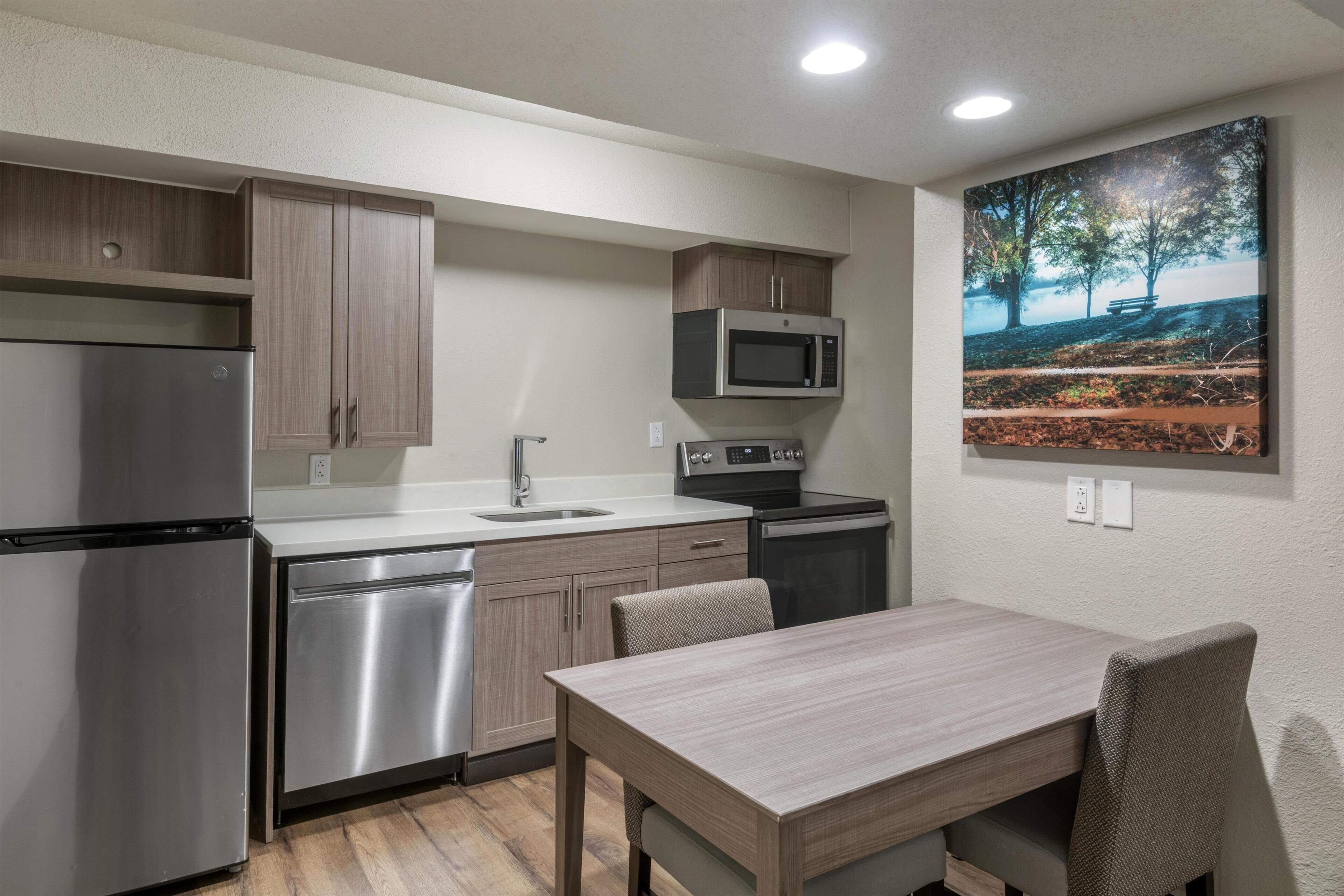 A compact kitchen with stainless steel appliances, a dining table, and a painting on the wall.