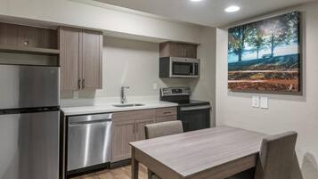 A compact kitchen with stainless steel appliances, a dining table, and a painting on the wall.