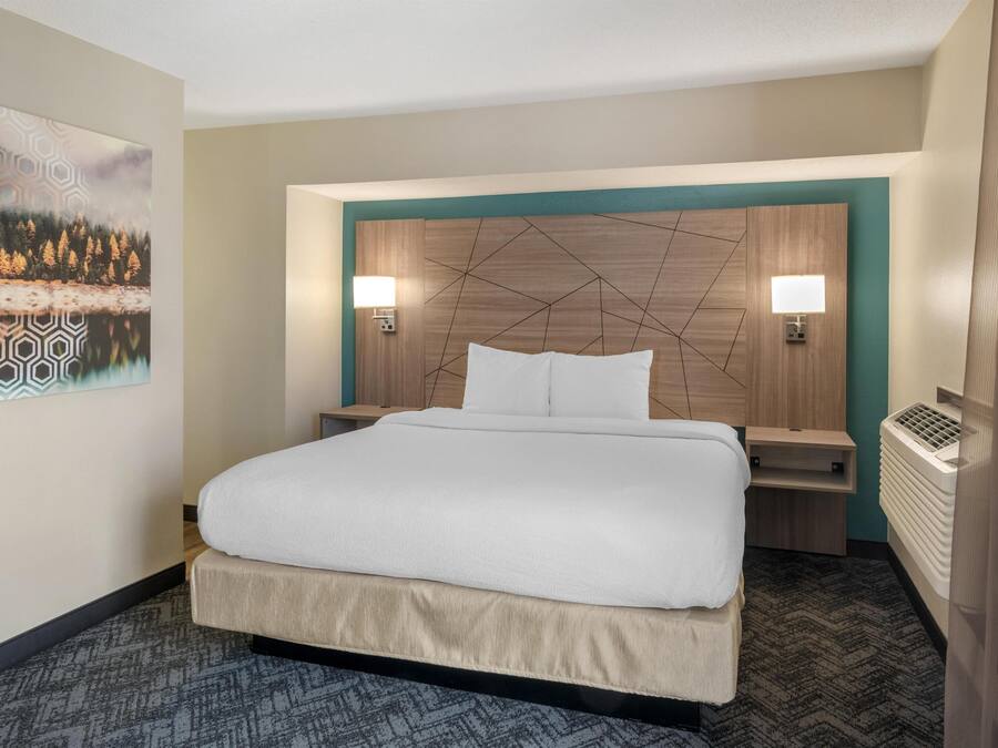 A hotel room with a large bed, two bedside tables, a wall-mounted lamp, and a radiator.