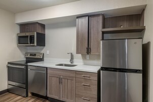 Una cocina moderna con electrodomésticos de acero inoxidable, armarios de madera y encimera blanca.