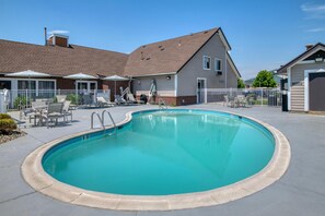 A swimming pool with lounge chairs, a fenced patio, and a building with a brick facade.