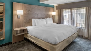 Une chambre d’hôtel avec un grand lit, une table de chevet, une lampe fixée au mur et une fenêtre avec des rideaux.
