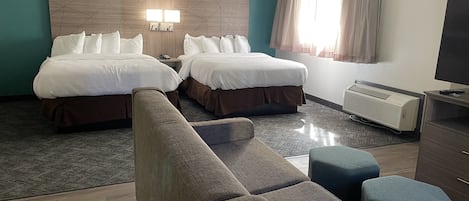 A hotel room with two beds, a sofa, a TV, and a heater.