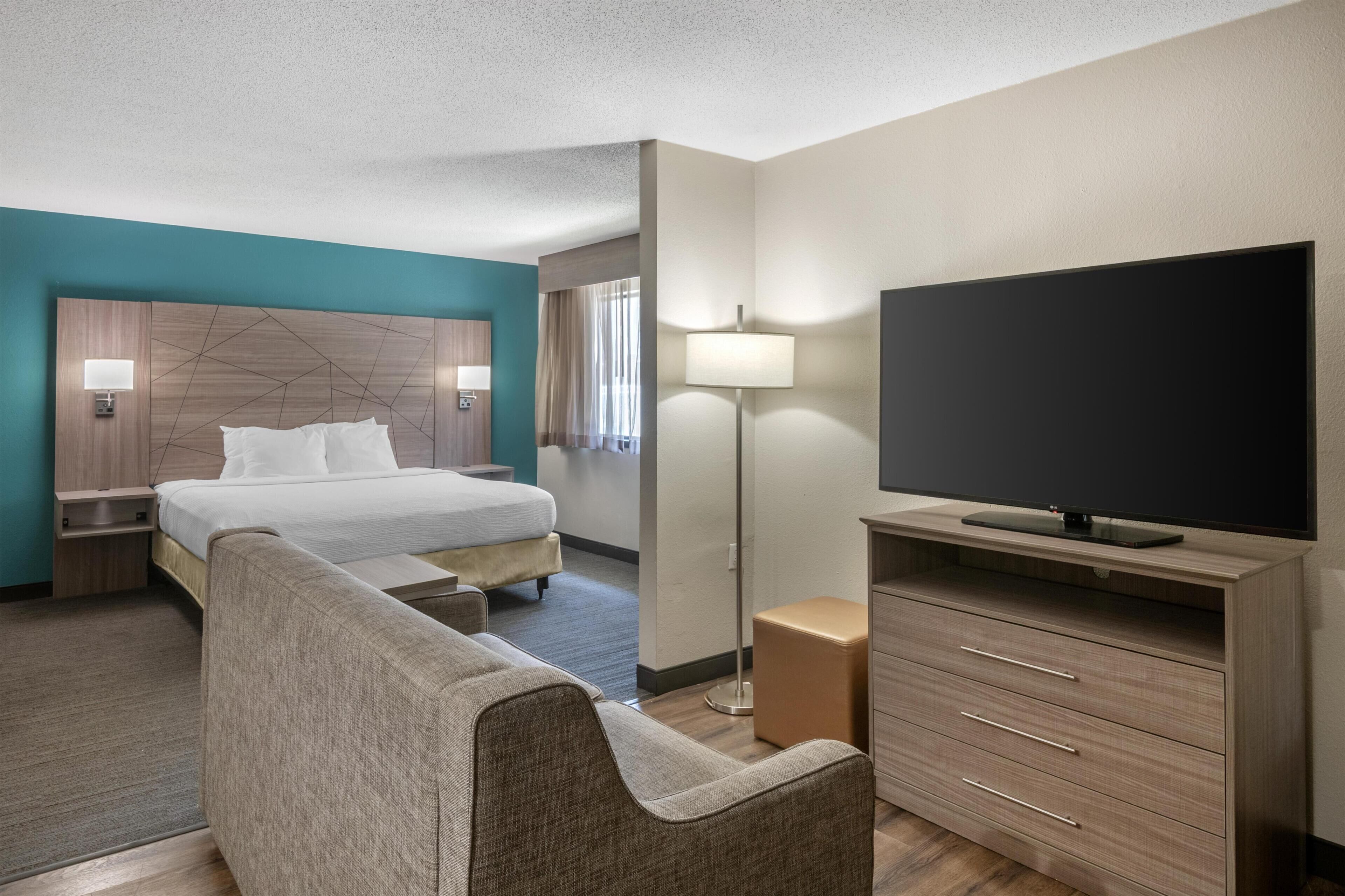 Una habitación de hotel con cama, televisión de pantalla plana, sofá, escritorio y lámpara.