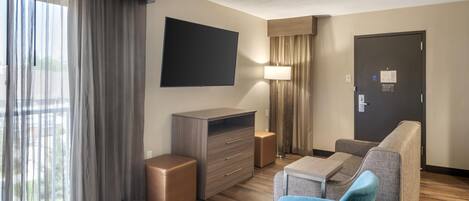 Habitación de hotel con televisión de pantalla plana, un sofá, una mesita, una lámpara, un armario y una puerta.