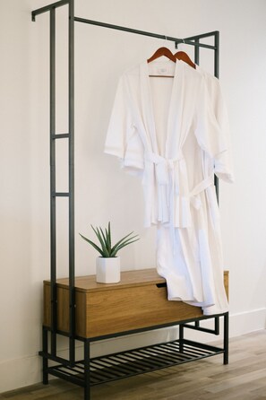 A wooden bench with a potted plant beside a metal rack holding a white robe.
