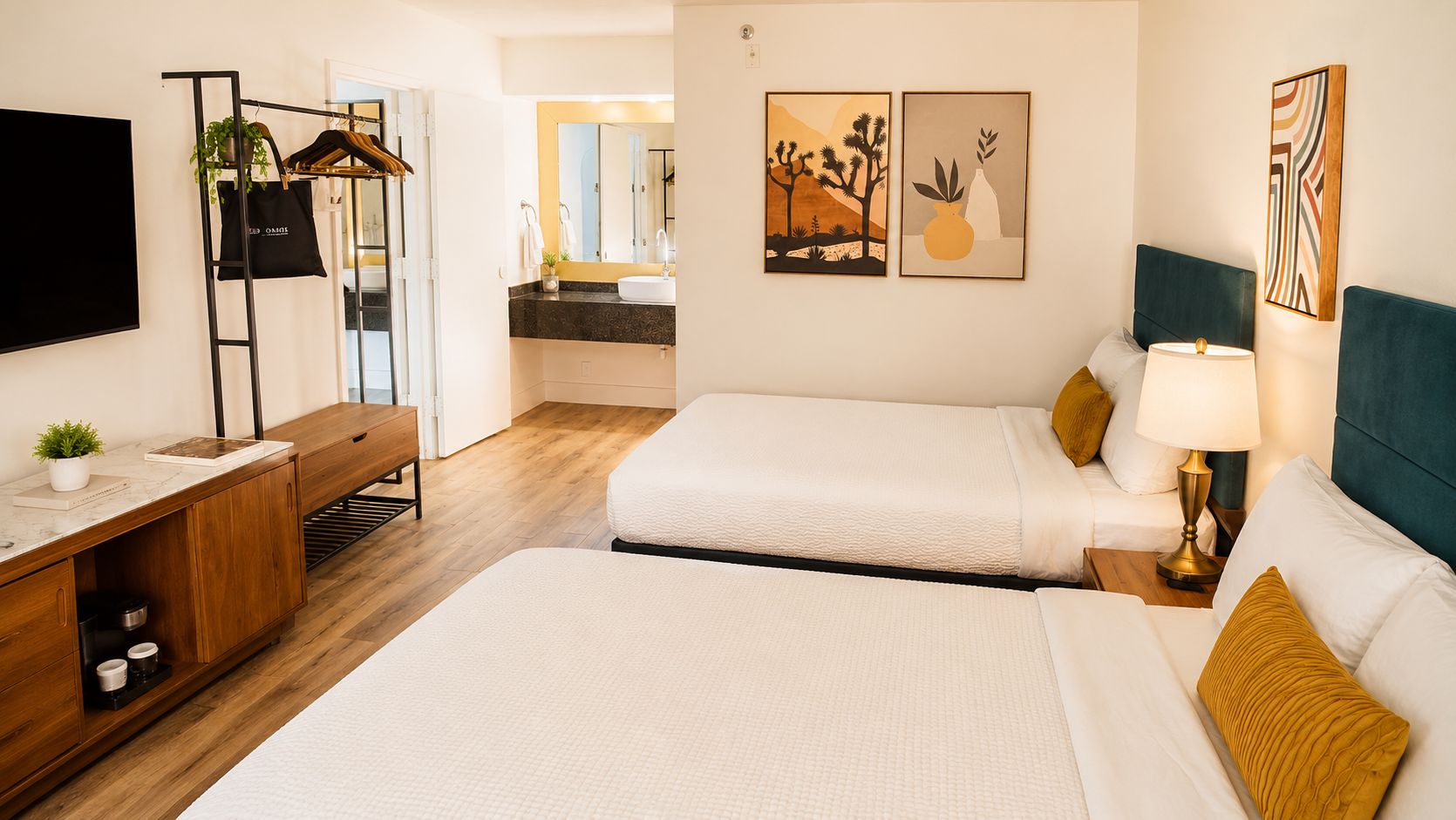 A hotel room with two beds, a desk, a TV, and artwork on the walls.