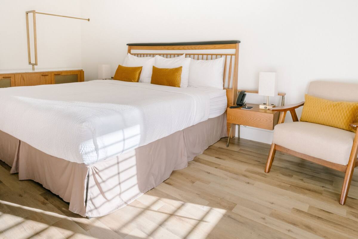 A hotel room with a large bed, bedside tables, a chair, and a nightstand with a lamp.