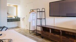 Habitación de hotel con cama, cómoda de madera, televisor, espejo, lavamanos y perchero.