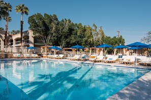 A swimming pool with lounge chairs and umbrellas, surrounded by palm trees and a building with balconies. - L3 Oasis Hotel (Palm Springs)