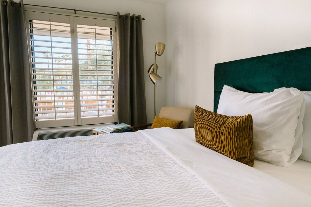 A hotel room with a large bed, a bedside lamp, a chair, and a window with curtains.