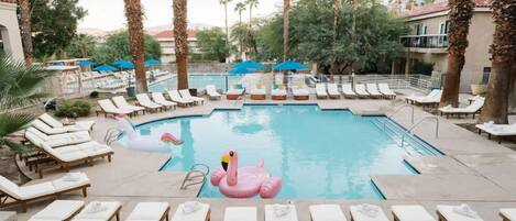 A pool area with lounge chairs, palm trees, and a flamingo float.