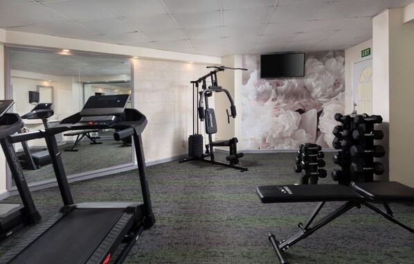 A gym with treadmills, weight machines, and a wall-mounted TV.