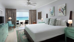 A hotel room with a bed, a desk, a chair, a TV, and a view of the ocean. - Mango Bay All Inclusive (Holetown)