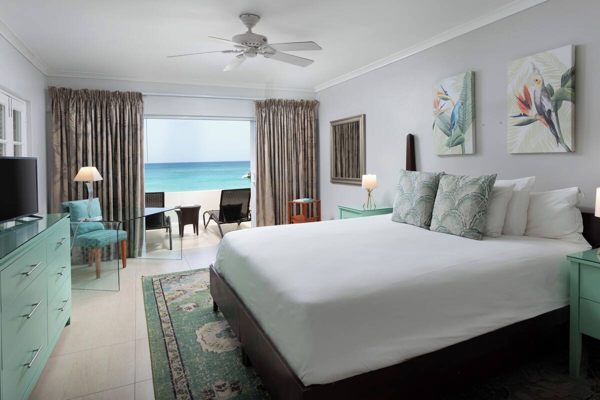 A hotel room with a bed, a desk, a chair, a TV, and a view of the ocean.