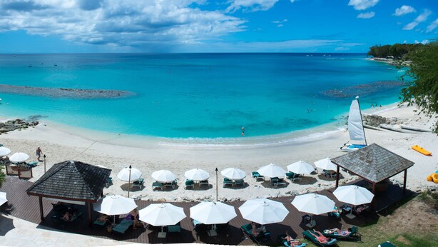 A beach resort with sun loungers, umbrellas, and a sailboat. - Mango Bay All Inclusive (Holetown)