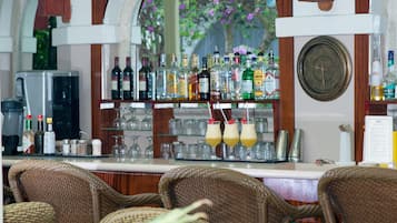 Una zona de bar con sillas de mimbre, una máquina de café y una variedad de botellas y vasos en estanterías.
