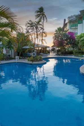 A swimming pool with lounge chairs and palm trees, surrounded by a building with a green facade.