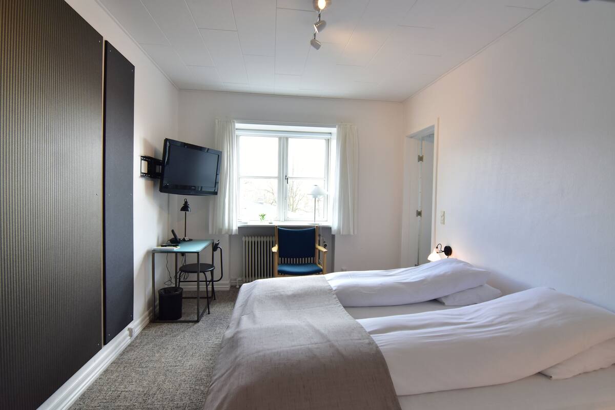 Een hotelkamer met twee bedden, een bureau met een computer, een stoel, een televisie en een raam met gordijnen.