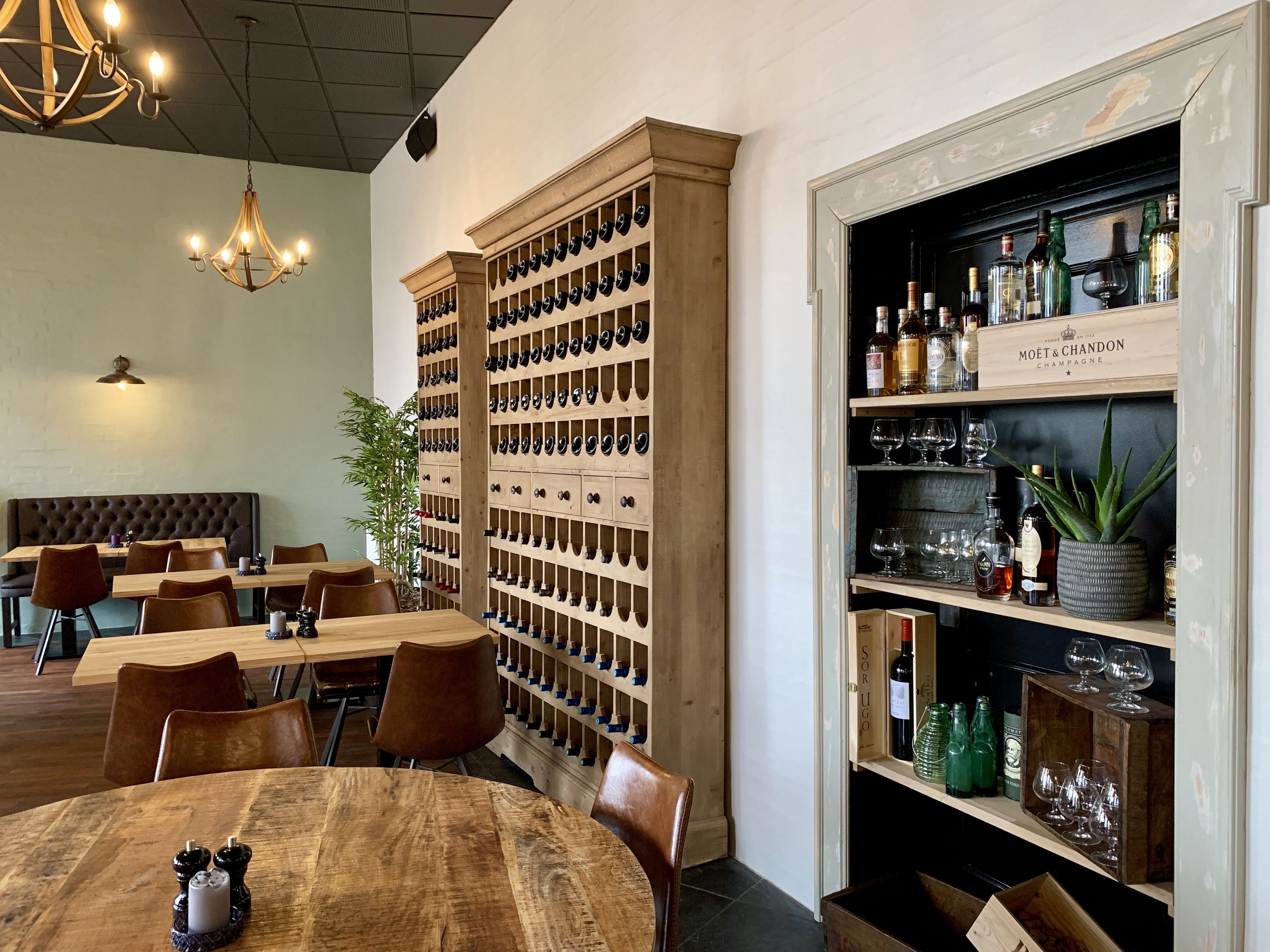 L’intérieur d’un restaurant, avec des tables et des chaises en bois, un présentoir à bouteilles de vin et un bar où sont exposées des bouteilles et des verres.