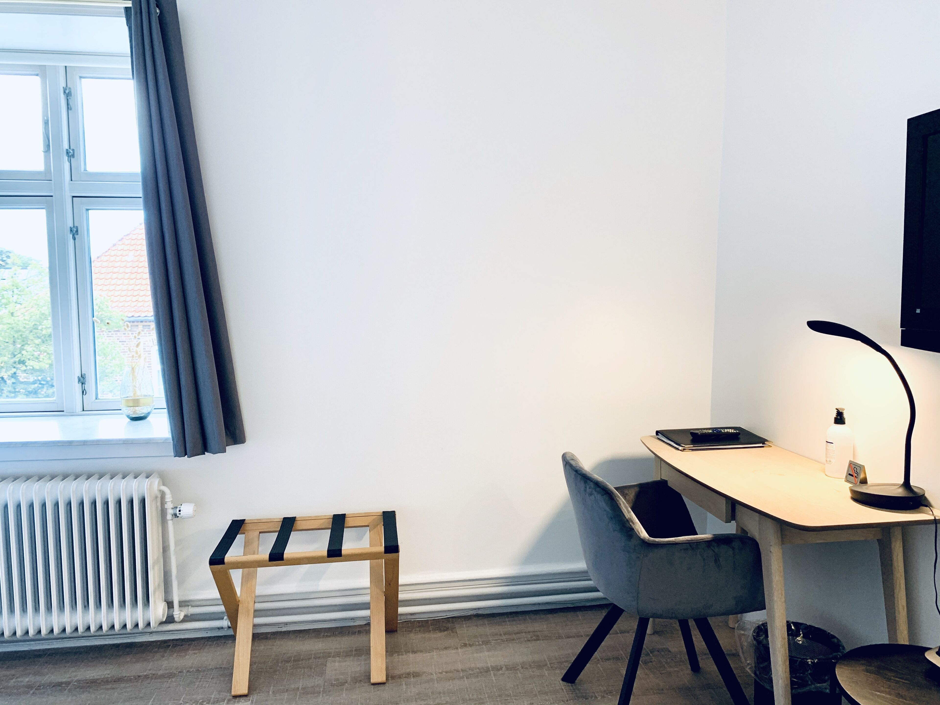 A room with a desk, chair, radiator, and a small bench.