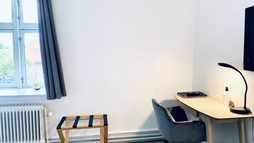 A room with a desk, chair, radiator, and a small bench.