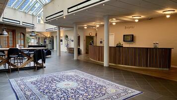En rummelig lobby med en receptionsdisk, en stor gulvtæppe med et mønster, og et ovenlys.